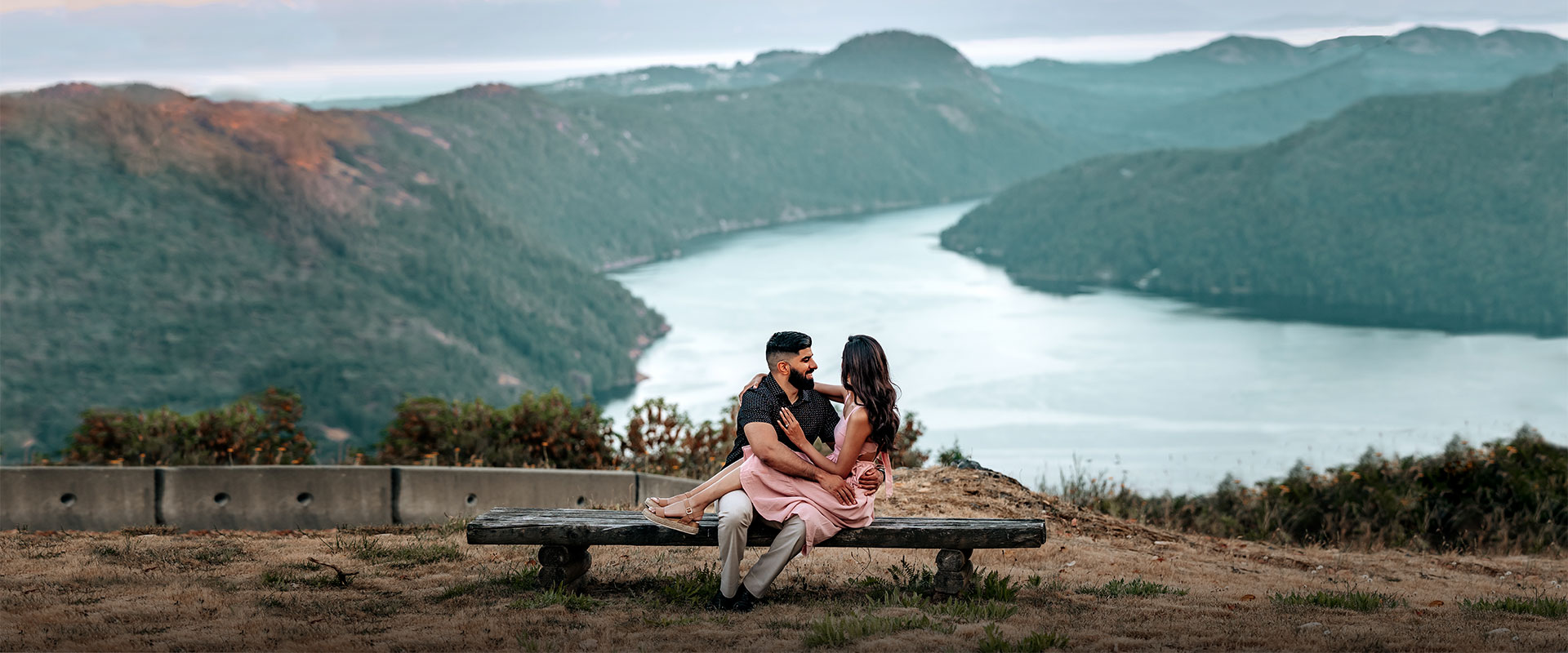 A man sitting on a bench with his wife in his arms with the Saanich inlet in the background.
