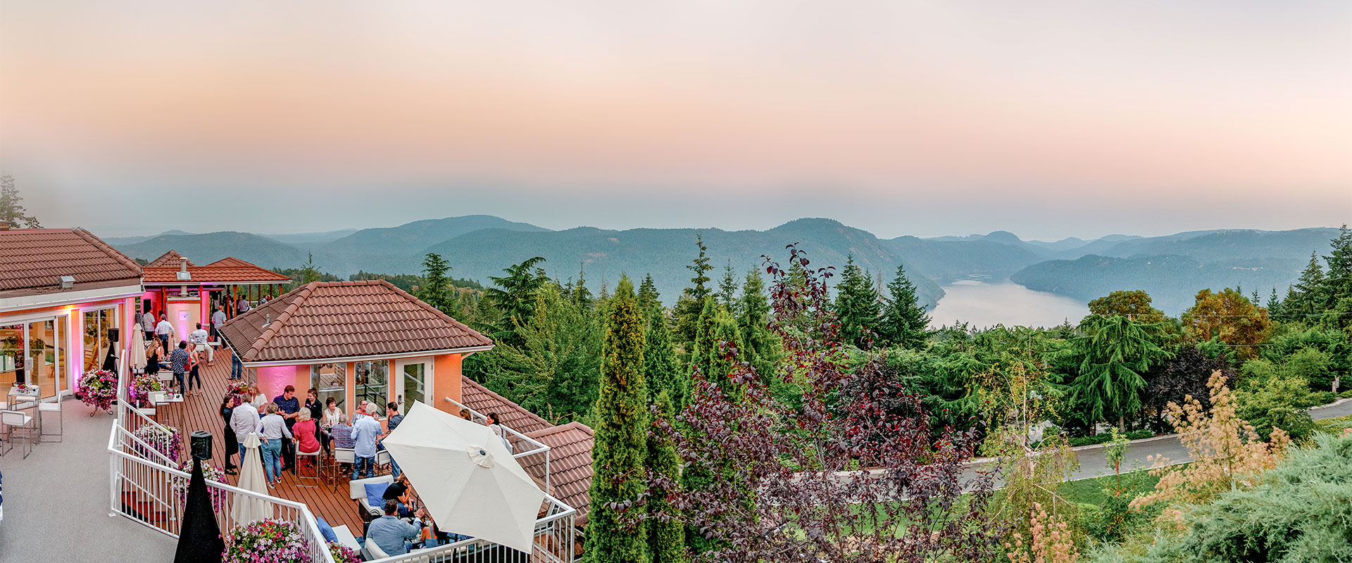 A group of happy people having a party on the patio of the Villa Principale overlooking the astonishing scenery of the Saanich inlet, the Malahat mountains, Mount Finlayson.